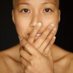 Cancer patient who has lost her hair stares confidently at the camera, surgery scars and main port visible on her chest.