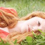 Portrait of a redheaded teenage girl lying in green grass