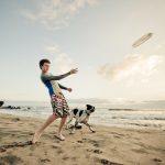 A teenage boy tosses a frisbee for two eager dogs on a quiet beach in Mexico.